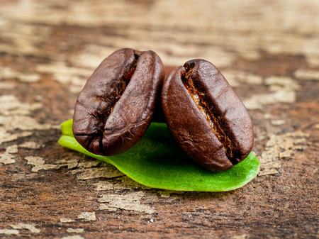 Coffee grains and green leaf on grunge wooden backgroundの写真素材