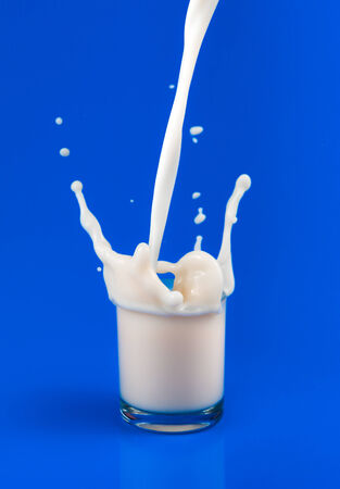 splash of milk in transparent glass on blue backgroundの写真素材