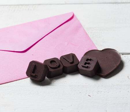 Chocolate heart with letter paper on the wooden background