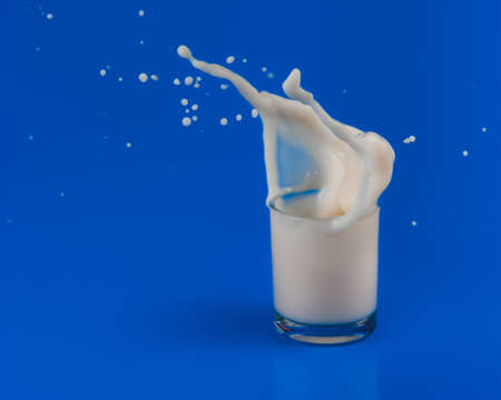 splash of milk in transparent glass on blue backgroundの写真素材