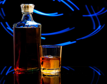 bottle and glass of whiskey with ice on dark background,curved glow lineの写真素材