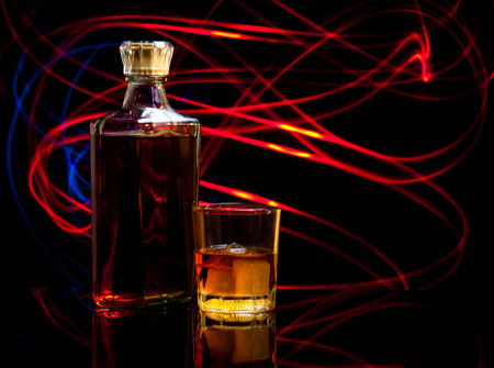 bottle and glass of whiskey with ice on dark background,curved glow line