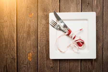 plate with a knife and fork wrapped in measuring tape on a wooden background. View from above
