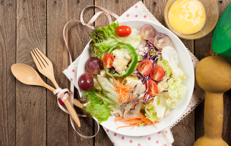 Dumbells, tape measure and healthy food salad on wooden background,View from aboveの写真素材
