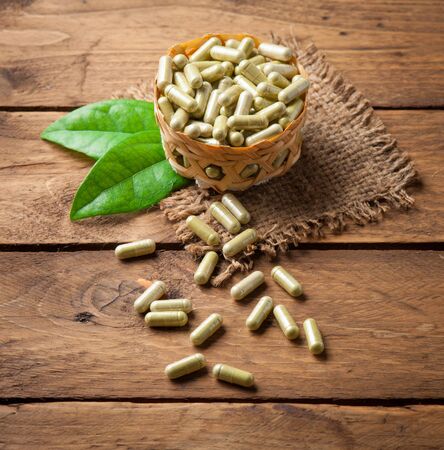 Herb capsules with green herbal leaf on woodの写真素材