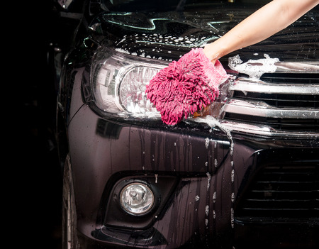 man washing a soapy black car with a clothの写真素材