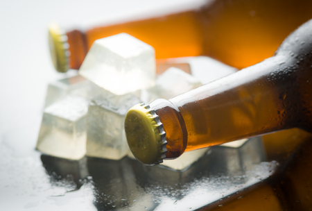 Glass bottles of beer with ice cubes on reflected glass backgroundの写真素材