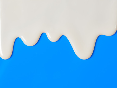 Dripping white milk, cream, paint yogurt on blue backgroundの写真素材