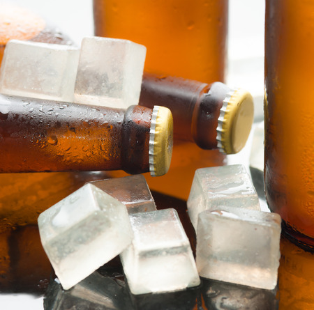 Glass bottles of beer with ice cubes on reflected glass backgroundの写真素材