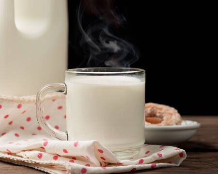 Hot milk in a glass with doughnut on woodの写真素材