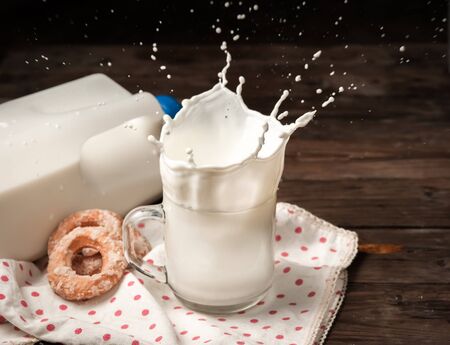 Splash of milk from the glass with doughnut on woodの写真素材