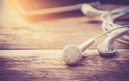 Earphones and Mobile phone on wooden background,vintage color toned imageの写真素材