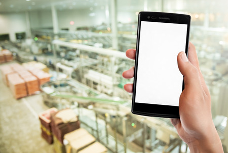 Hand holding smart phone on Manufacturing factory blurred background.の写真素材