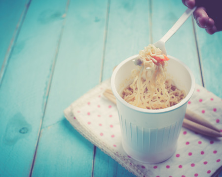 Concept of instant food,Instant noodle cup on blue wood table,vintage color toned imageの写真素材