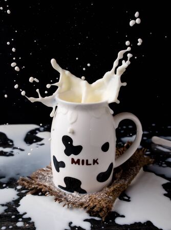 Splash of milk from the milk glass with cow camouflage on dark backgroundの写真素材