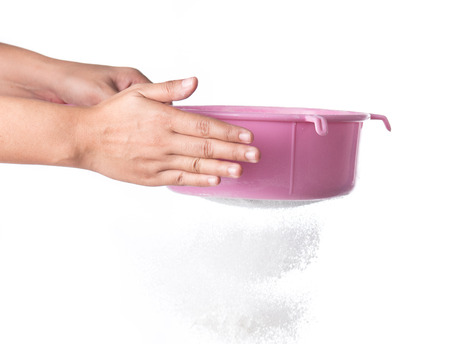 Flour sifting through a sieve for a baking isolated on whiteの写真素材