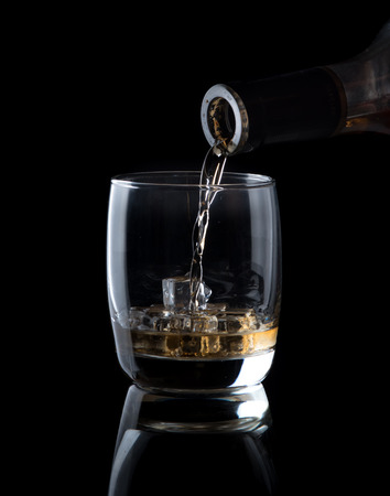 Pouring whiskey into glass  isolated on black backgroundの写真素材