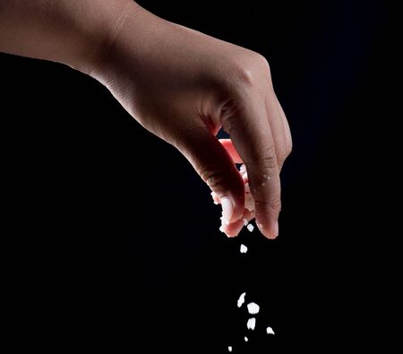Hand sprinkling salt over black background.の写真素材