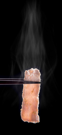 Sukiyaki or Shabu shabu pork slice in chopsticks with smoke isolated on black.の写真素材