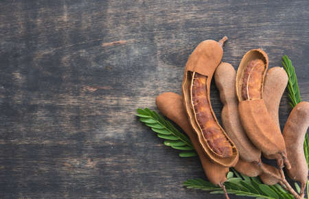 Sweet ripe tamarind pods with tamarind leaves on wood background,top viewの写真素材