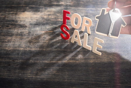 Symbol of the house with text FOR SALE and key on wooden background,human's finger