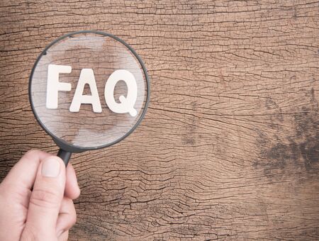 Hand holding magnifying glass on wood letters as FAQ abbreviation, frequently asked questions on wooden background.の写真素材