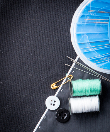 needles, cotton reels and buttons on black fabric
