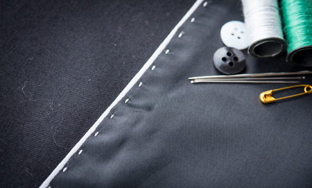 needles, cotton reels and buttons on black fabricの写真素材