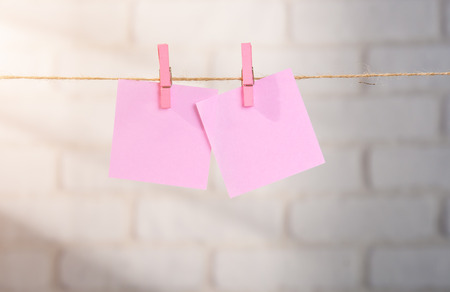 Wooden clothespin and blank paper on a rope against white brick wall