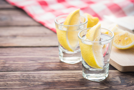 Vodka with lemon in shot glass on wooden backgroundの写真素材