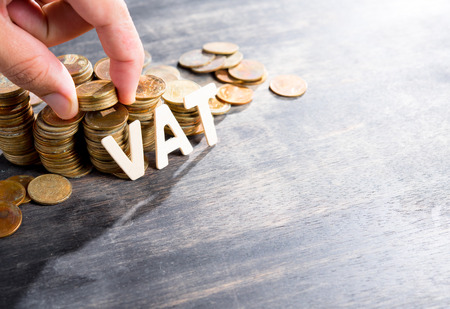 VAT wood word with stacked coins on dark wooden background, human's finger at coinsの写真素材