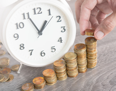 Finance and Money concept,Hand hold money coins and alarm clock on wood table