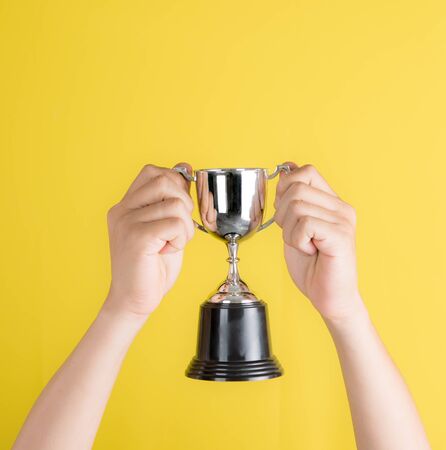 Hand holding silver trophy with text space against yellow backgroundの写真素材