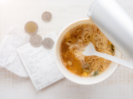 Instant noodle cup with coin on wooden table,Concept end of month not enough moneyの写真素材