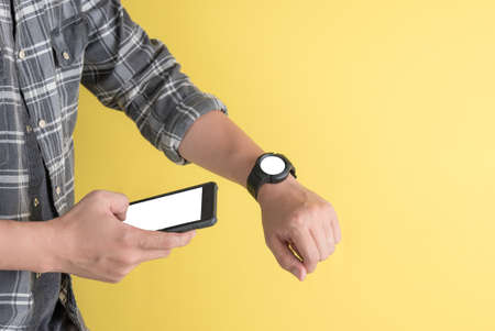 Male hands with smartphone and smart watch with blank screens on yellow background.