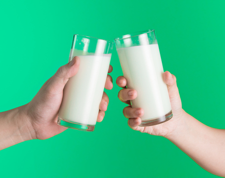 Two hands holding glass of milk on green background,Clinking glasses of milkの写真素材