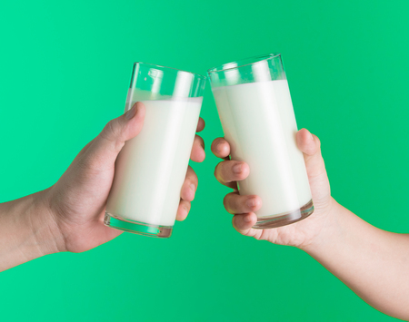 Two hands holding glass of milk on green background,Clinking glasses of milk