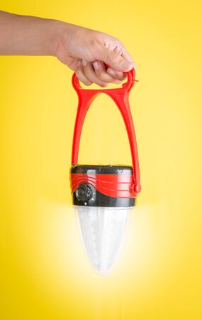 Hand holding a LED lantern lamp against yellow backgroundの写真素材