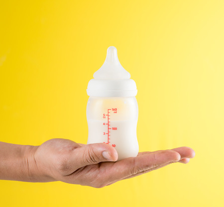 Hand holding a baby bottle of milk on yellow backgroundの写真素材