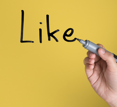 Hand holding black permanent marker and writing word "Like"against yellow backgroundの写真素材