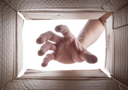 Man is stretching hand into cardboard box,View from the boxの写真素材