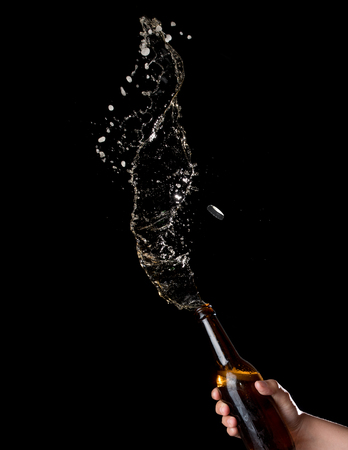 Gold beer bottle opening with exploding and splashing on dark backgroundの写真素材