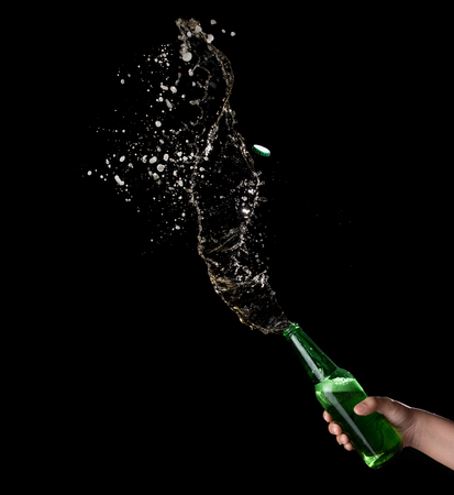 Green beer bottle opening with exploding and splashing on dark backgroundの写真素材