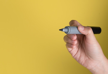 Hand holding a black marker with text space against yellow backgroundの写真素材