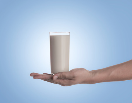 Hand holding glass of milk on blue backgroundの写真素材