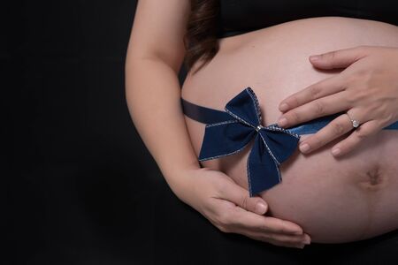 pregnant woman tummy with blue ribbon over blackの写真素材