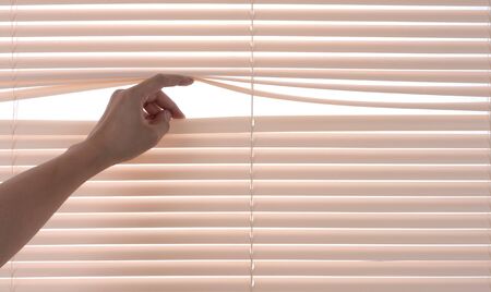 Windows jalousie,hand separating slats of venetian blinds with a finger to see throughの写真素材
