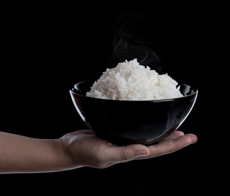 Hand holding a bowl with cooked rice on black backgroundの写真素材
