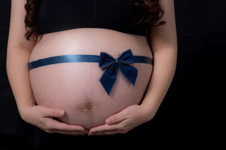 pregnant woman tummy with blue ribbon over blackの写真素材