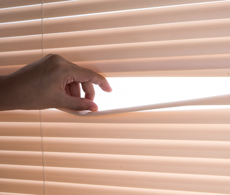 Windows jalousie,hand separating slats of venetian blinds with a finger to see throughの写真素材